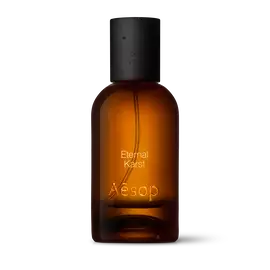 Amber glass Aesop Eternal Karst Eau de Parfum bottle with black cap on a white background.