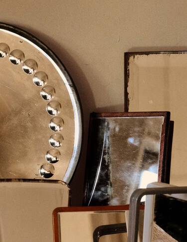 Stacked metallic and stone objects in bronze, beige and dark brown tones, arranged as overlapping geometric forms against a neutral wall.