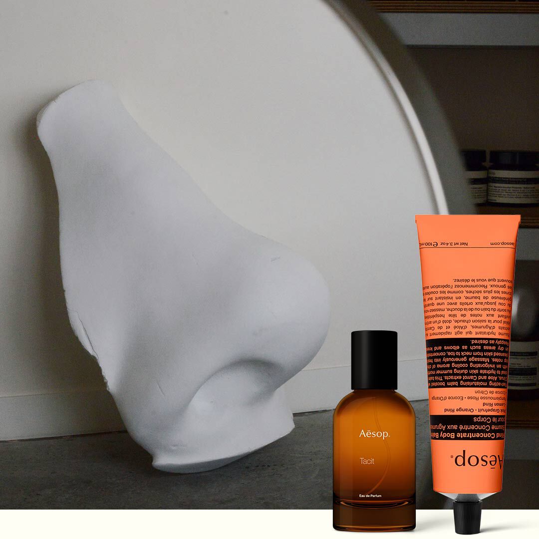 Amber perfume bottle and coral hand cream beside a white sculpture