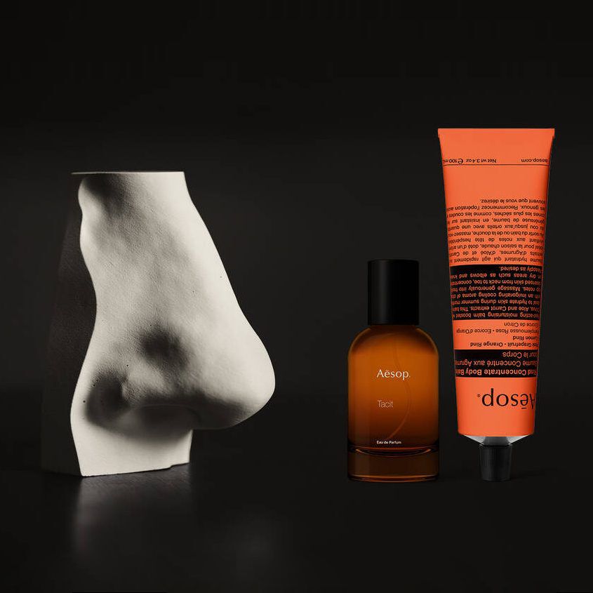 Amber perfume bottle and coral hand cream beside a white sculpture.