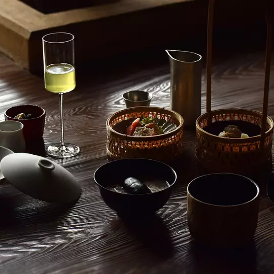 A dark, textured wooden table with various Japanese dishes and an elegant stemmed glass.