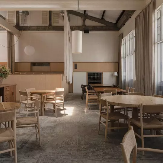 An empty restaurant with high ceilings, timber tables and chairs, and hanging pendant lights.